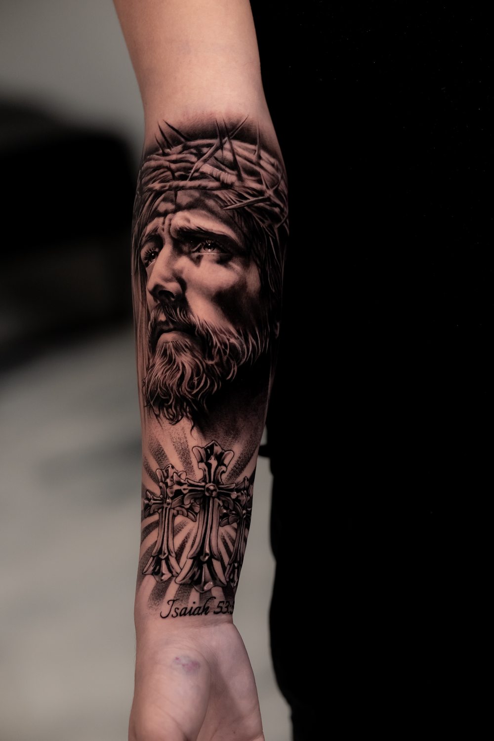 Black and grey religious tattoo of Jesus and a cross on a forearm