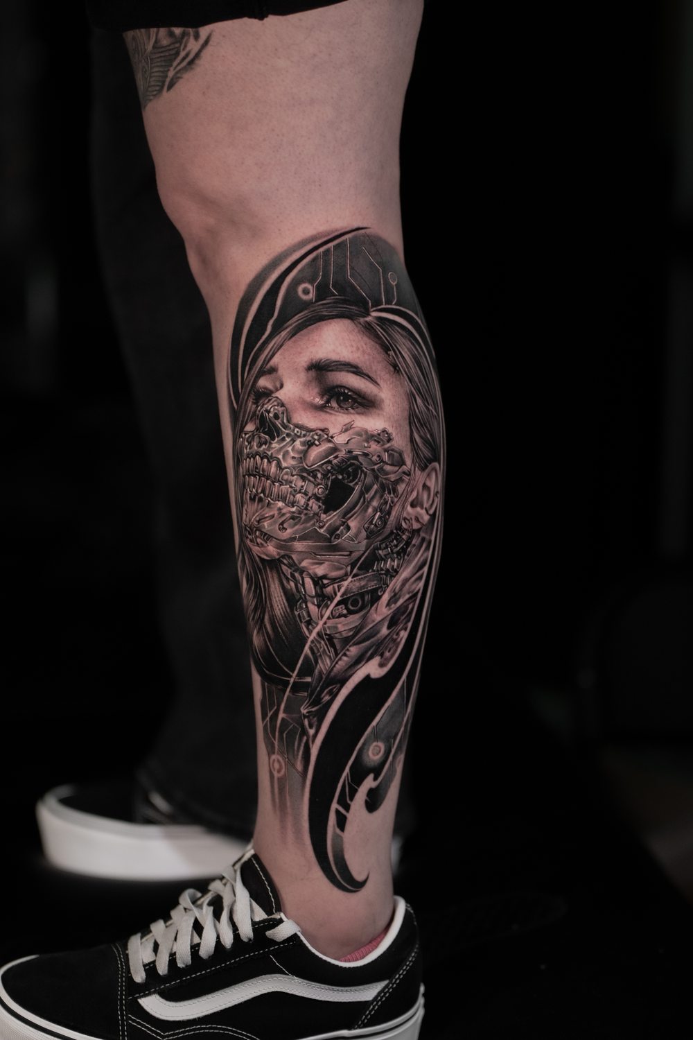 Black and grey biomechanical portrait tattoo on a calf
